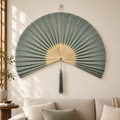 Sage green woven wall fan with gray tassel above a living room sofa